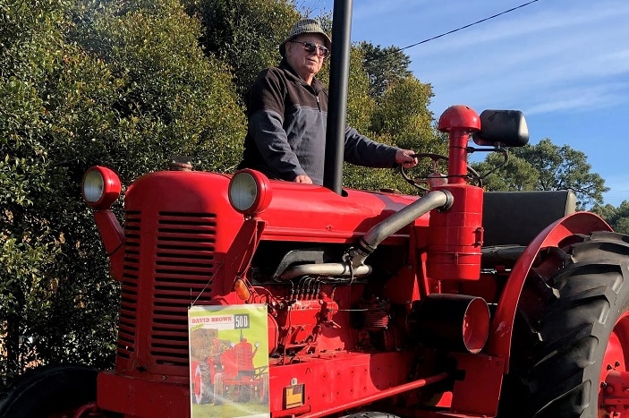 A bright red tractor emits exhaust fumes while a man sits on top.