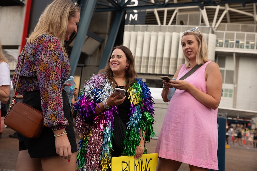 Woman in rainbow tinsel beams as she talks to two women