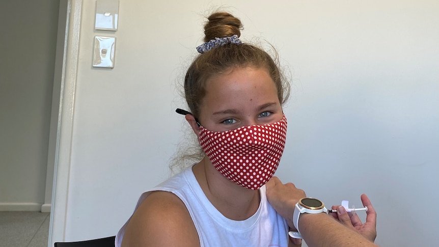 A girl looks at the camera wearing a mask as she gets vaccinated
