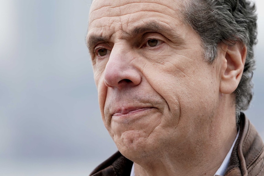 A close up photograph shows the lined face of a middle aged man with short hair.