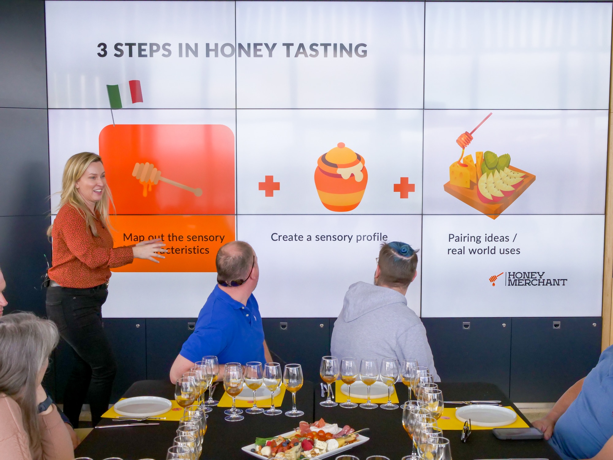 A woman points to pictures of honey on an electronic screen on a wall. 