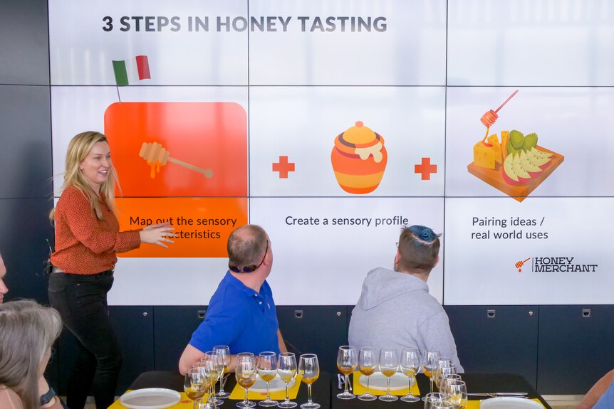 A woman points to pictures of honey on an electronic screen on a wall. 