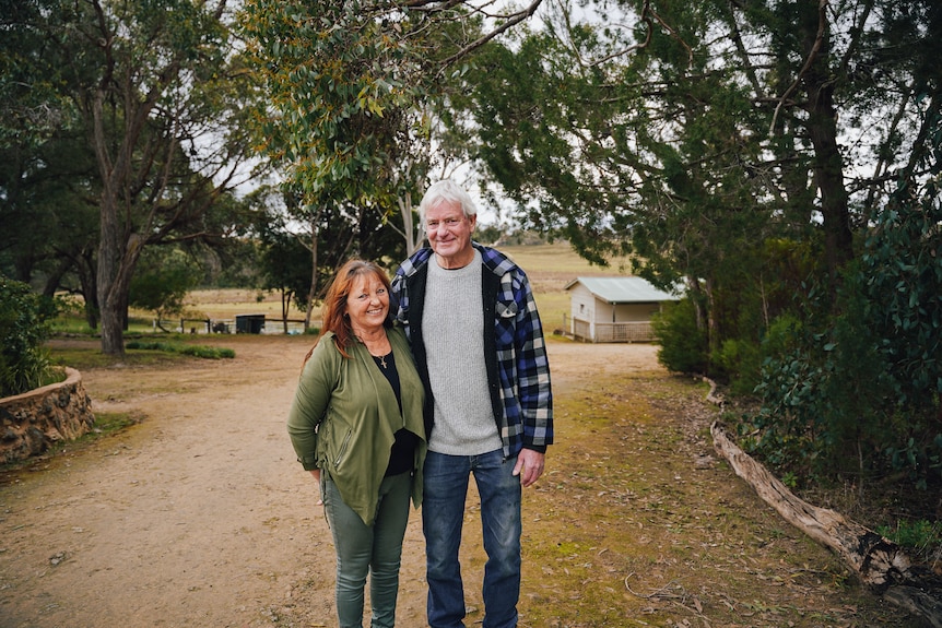 A man and woman stand on a dirt road surrounded by trees and laugh.