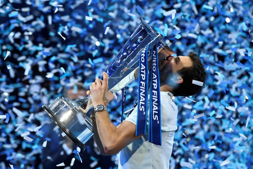 Grigor Dimitrov kisses the ATP Finals trophy as confetti rains down on the court.