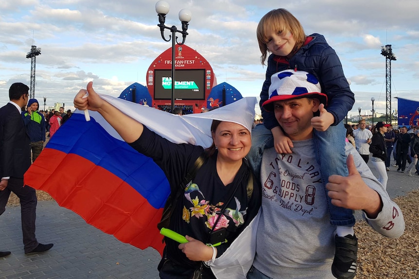 Woman and man, with a child on his shoulders, give the thumbs up