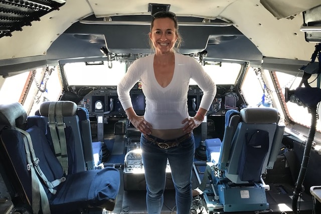 A woman stand with her hands on her hips inside an aircraft.
