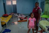 A woman and little girl stand in a room crowded with mattresses on the floor