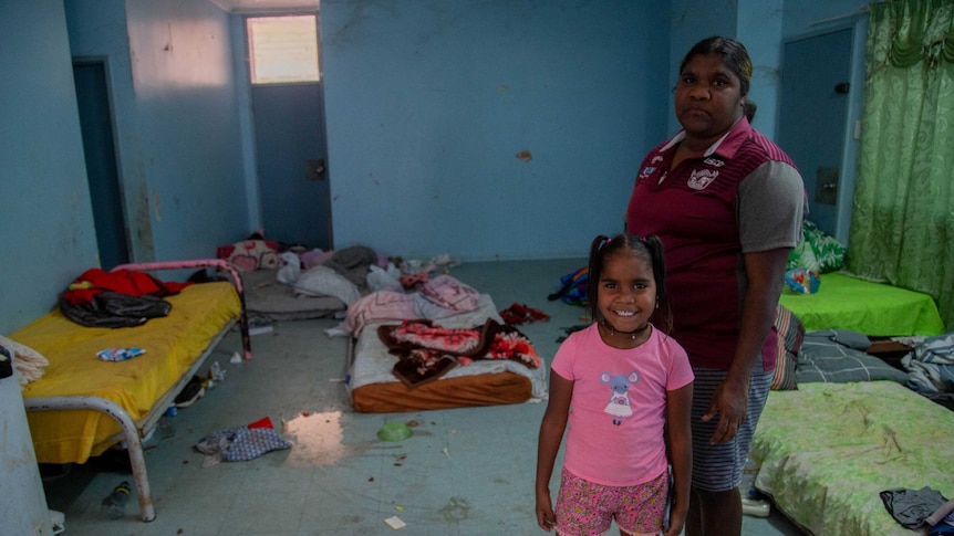 A woman and little girl stand in a room crowded with mattresses on the floor