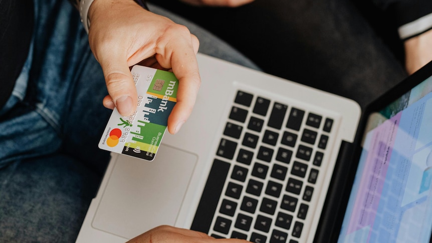 Person holding out a credit card card against their laptop