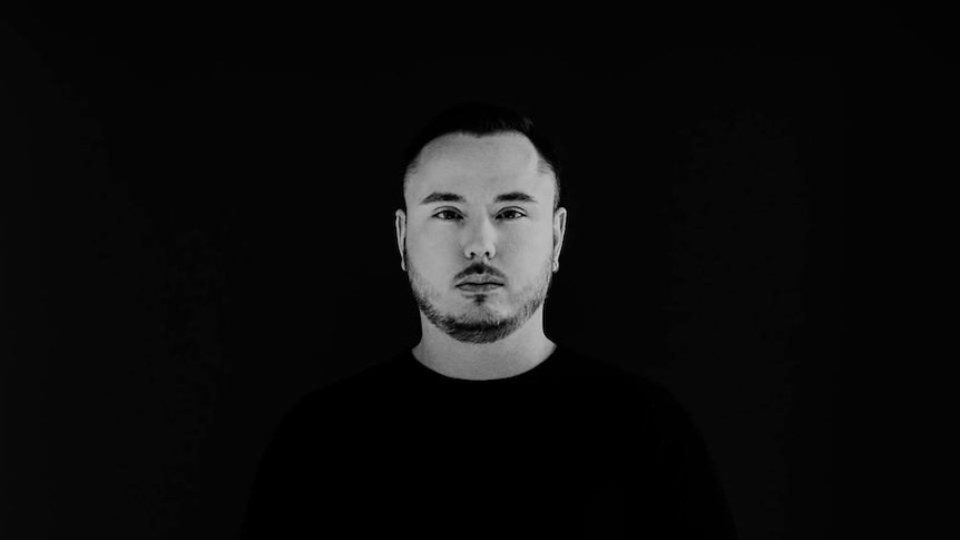 black and white pic of duke dumont standing infront of a black wall with a black jumper on staring dead pan at the camera