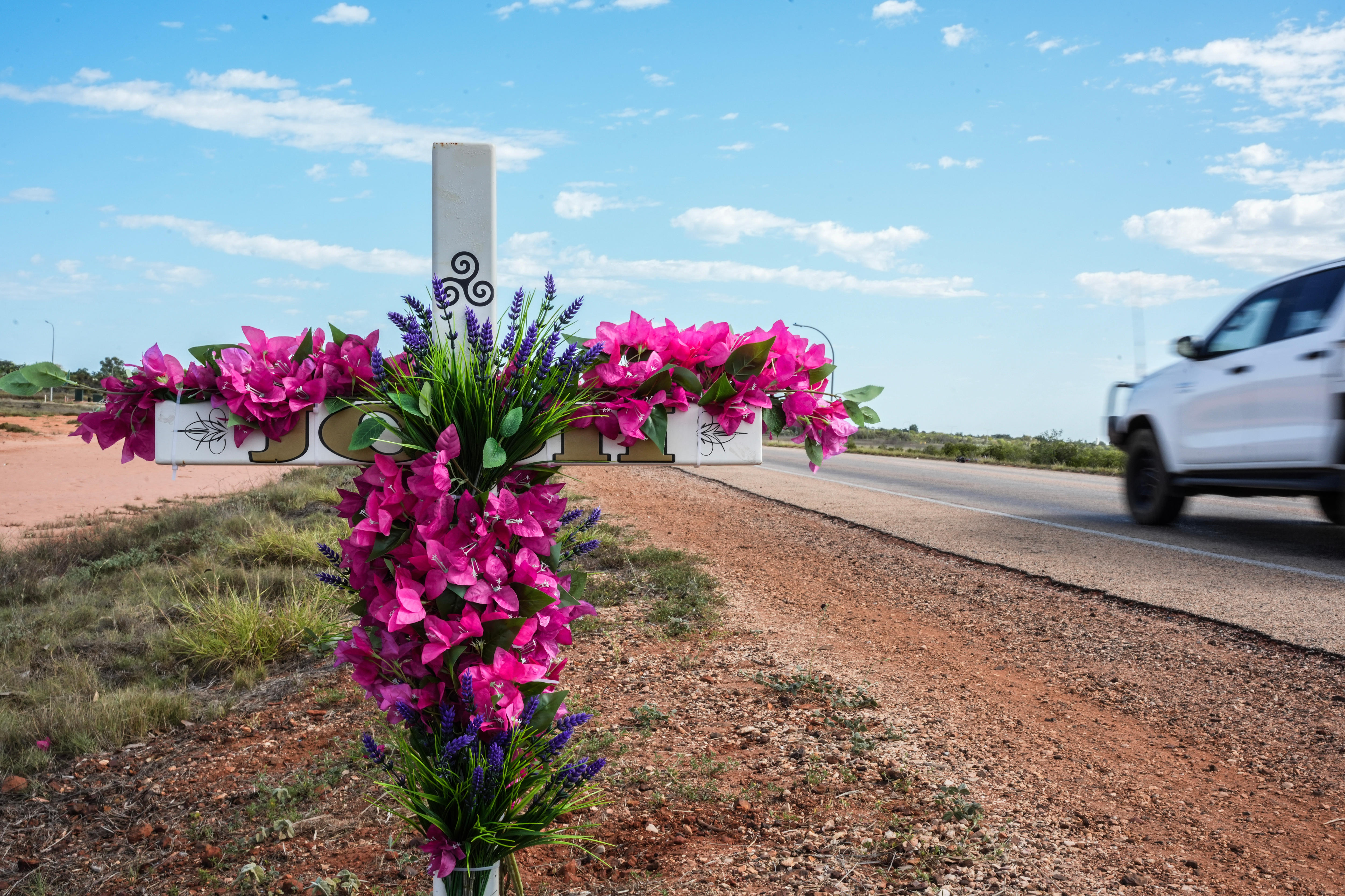 a memorial cross with flowers on a road 