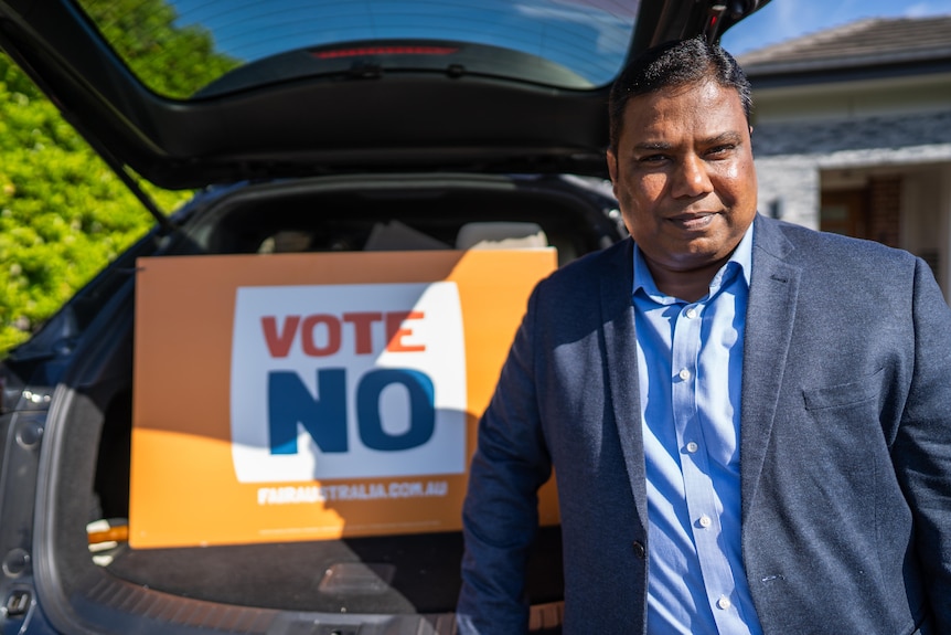 A man stands in front of a vote No sign.