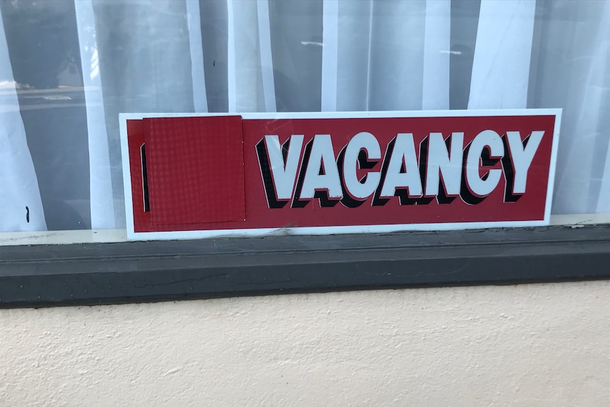A red sign in a window with a curtain behind, it reads 'vacancy'