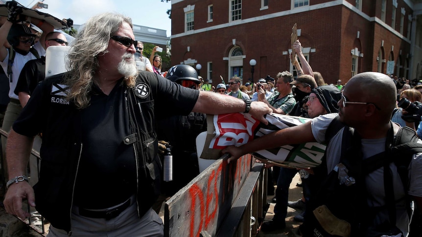 A large white man pulls a 'black lives matter' sign away from a black man.