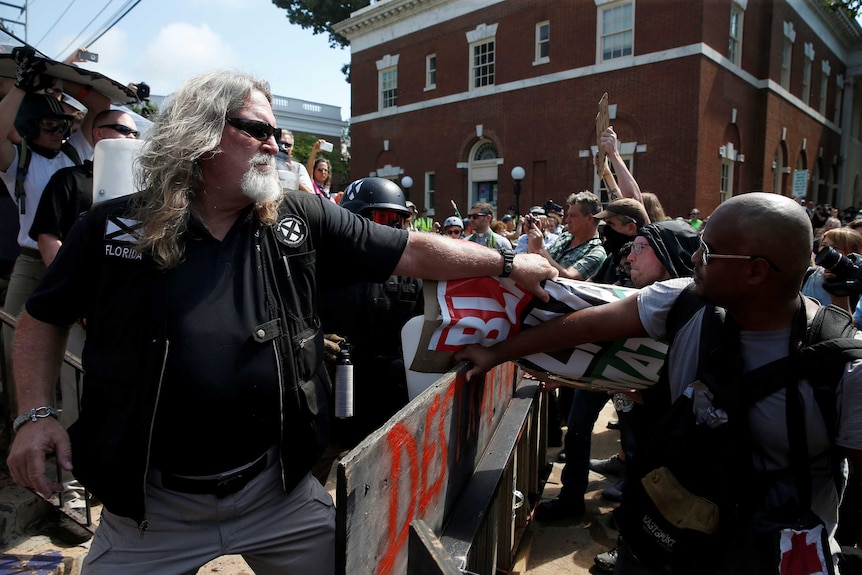 A large white man pulls a 'black lives matter' sign away from a black man.