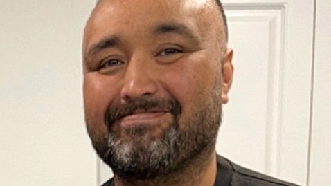 Man in black shirt with green emblem smiles at camera.