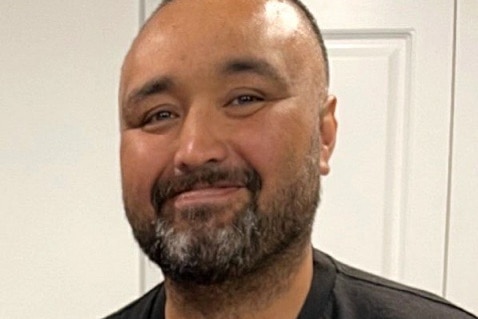 Man in black shirt with green emblem smiles at camera.