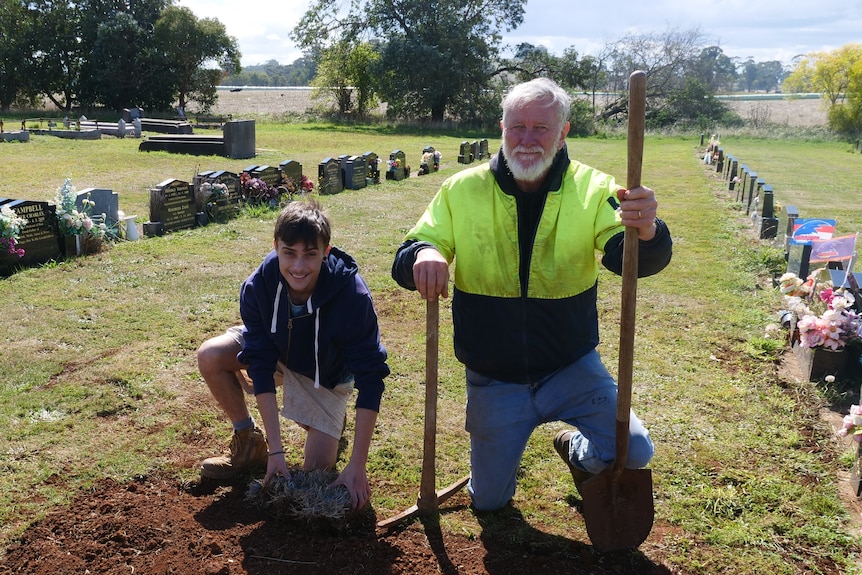 man and young man kneeling in a graveyard