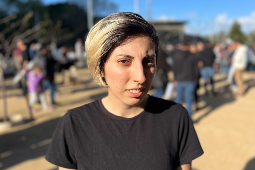 Deniz looks at the camera, in a black t-shirt standing in front of protesters.