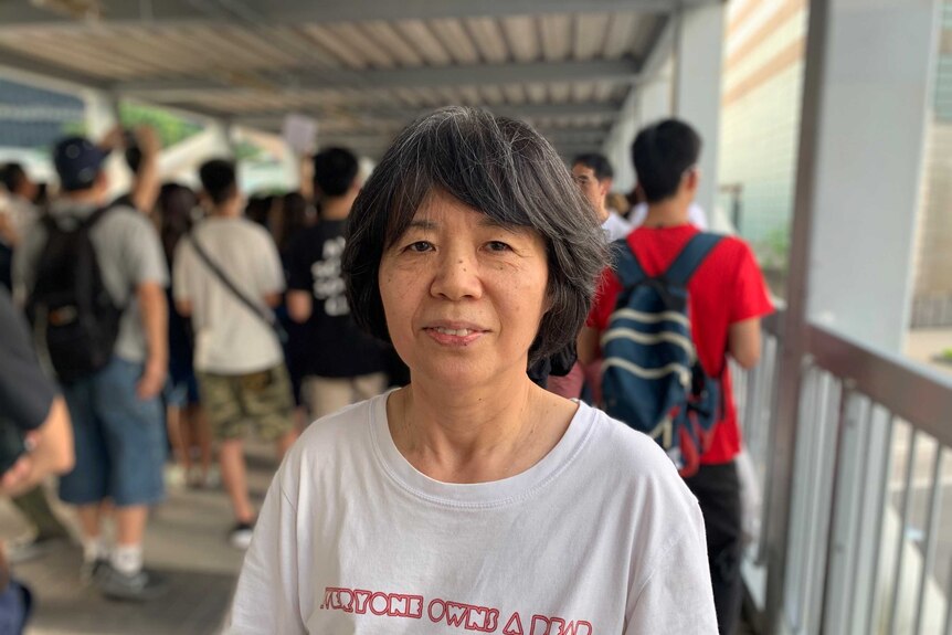 A woman with greying hair looks past the camera with a white t-shirt that reads 'everyone owns a dear'.