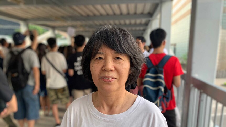 A woman with greying hair looks past the camera with a white t-shirt that reads 'everyone owns a dear'.