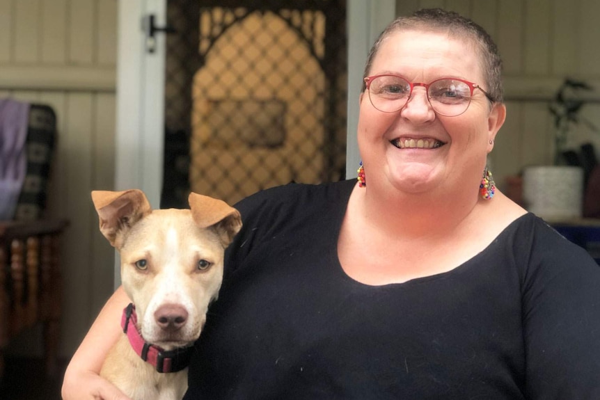 Sandy Walker smiles as she cuddles her dog outside a house.