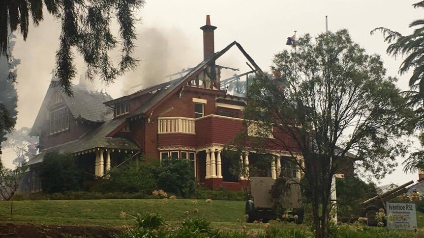 Smoke surrounds a two-storey brick building with its roof caved in after a large fire.