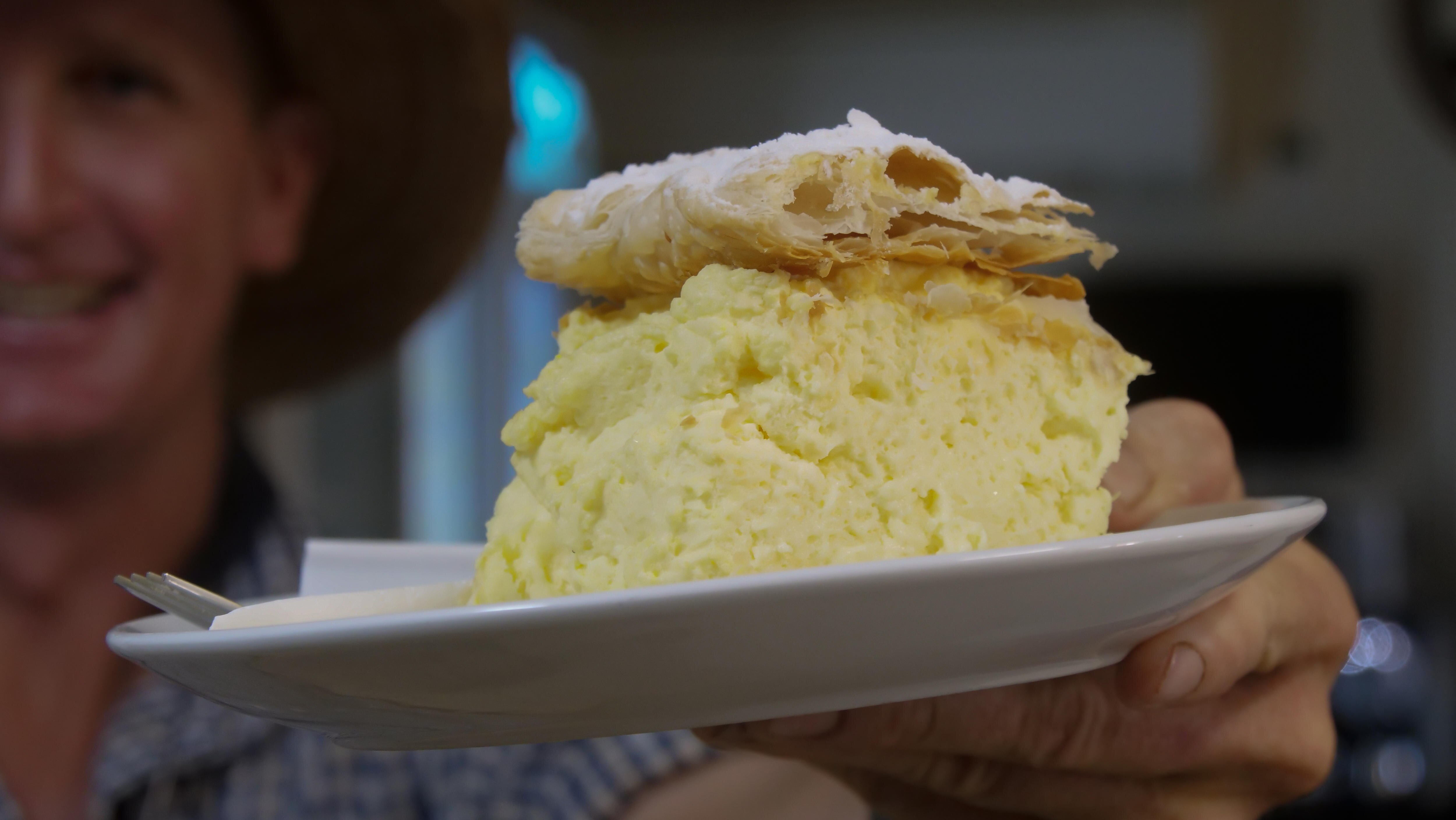 A crosssection of vanilla slice on a plate with a mans blurred face in the background
