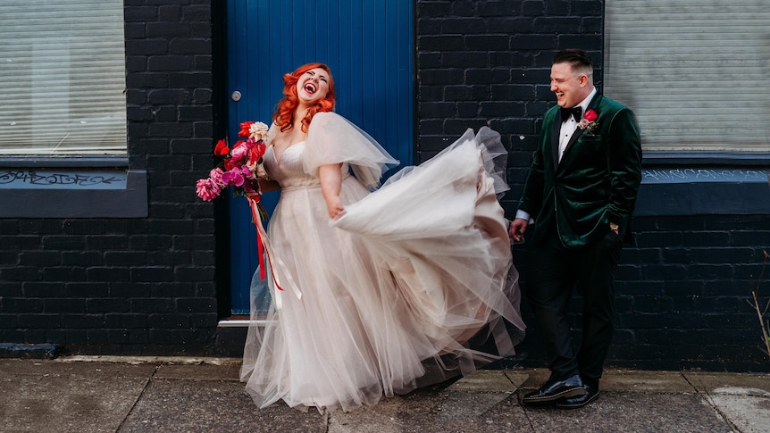 Couple in wedding outfits stands in the doorway 