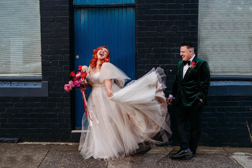 Couple in wedding outfits stands in the doorway 