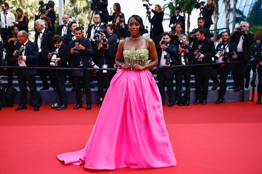 Aja Naomi King wearing a big silky bright pink skirt with a beaded green crop top with dangling beads