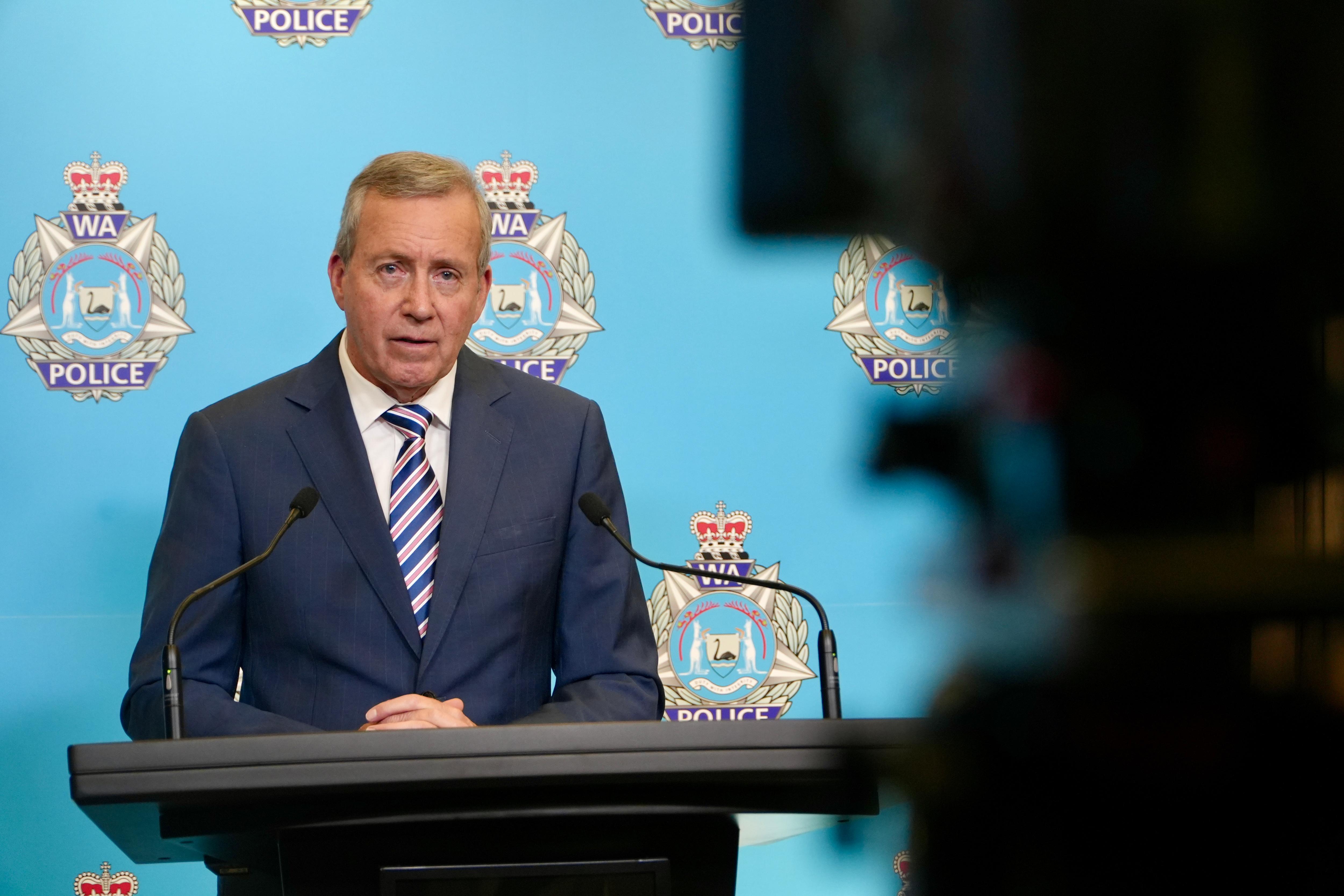 WA Police Minister Reece Whitby at a media conference inside WA Police headquarters, with a TV camera shadow to the right.