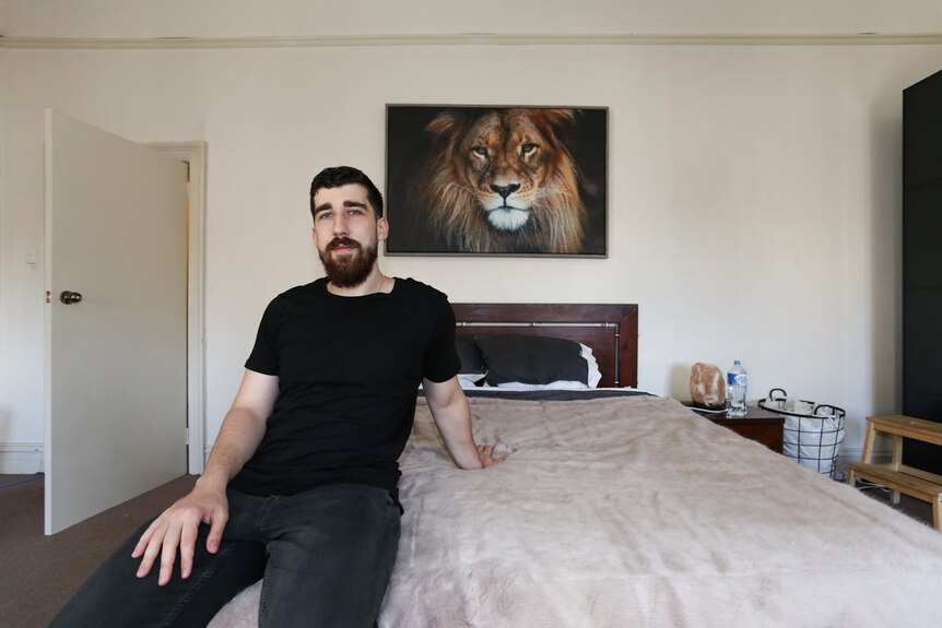 Sean Mallard sitting on the edge of his bed with a large painting of a lion above his bed.