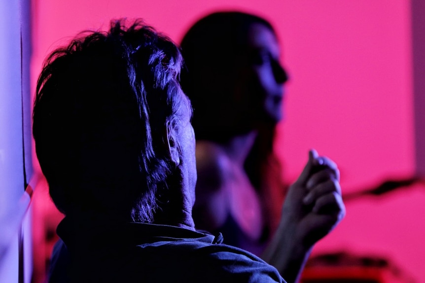 A man speaks to a woman with a red light behind.