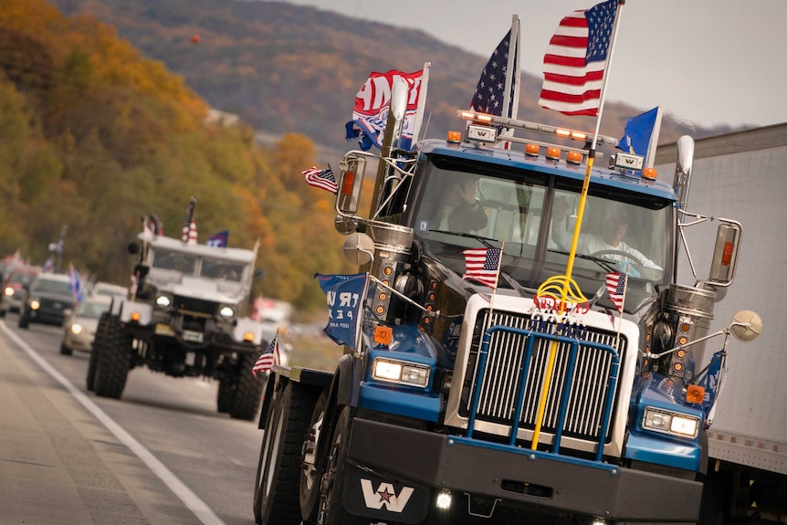 A truck driving down a freeway covered in US and Trump flags