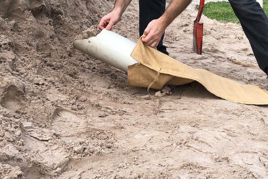 A close-up picture of a person filling a sandbag with a shovel in the background.