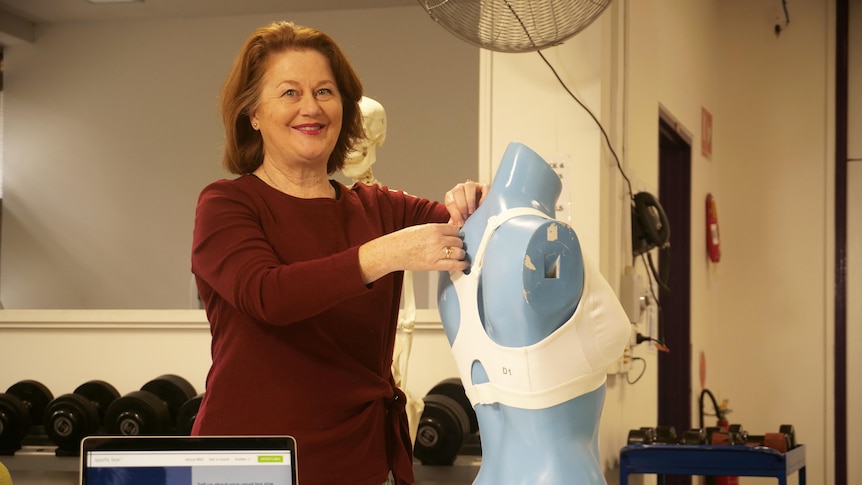 A smiling woman with long, dark hair fits a white sports bra on a blue mannequin.