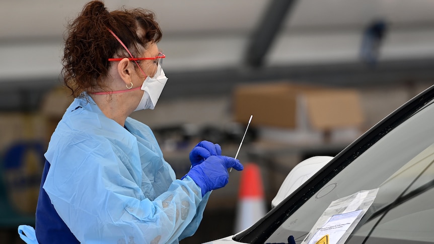 a woman wearing a mask and personal protective clothing holding a swab