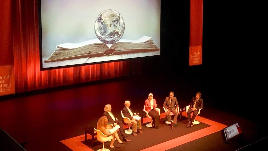 Panel sit gathered together on a stage in auditorium