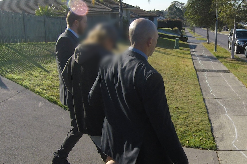The back of two detectives wearing suits holding a man with handcuffs on either arm