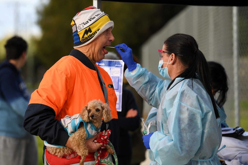 A man in an orange shirt and colourful hat holding a dog gets tested for COVID-19.