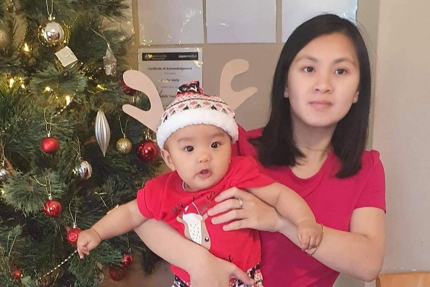 a woman and a baby standing in front of a christmas tree