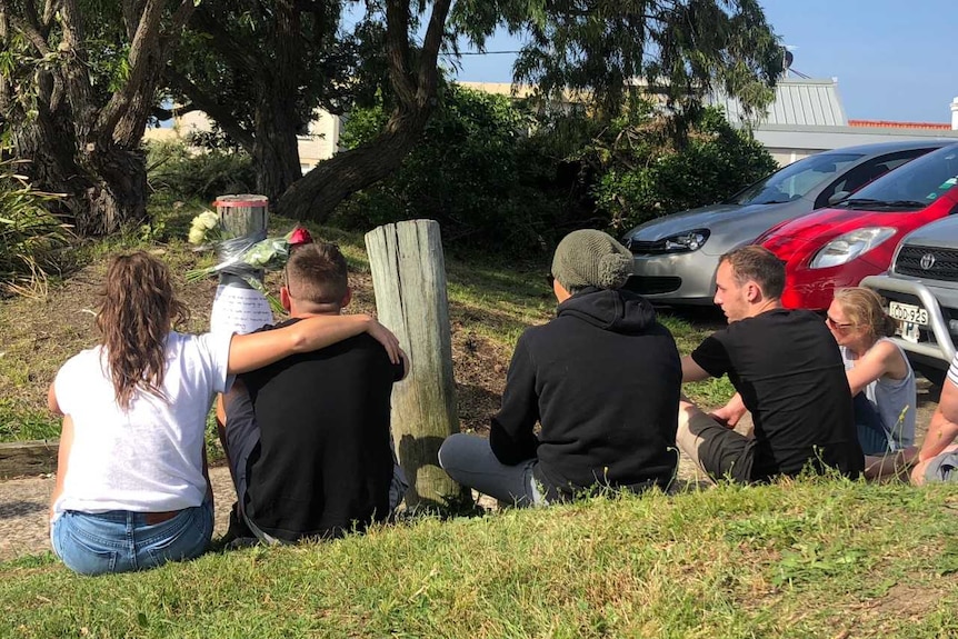 Five people sitting in front of a reserve with flowers next to a post