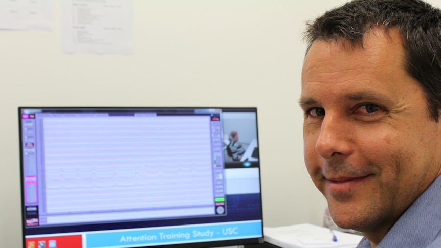 man sits in front of a computer screen showing brain waves.