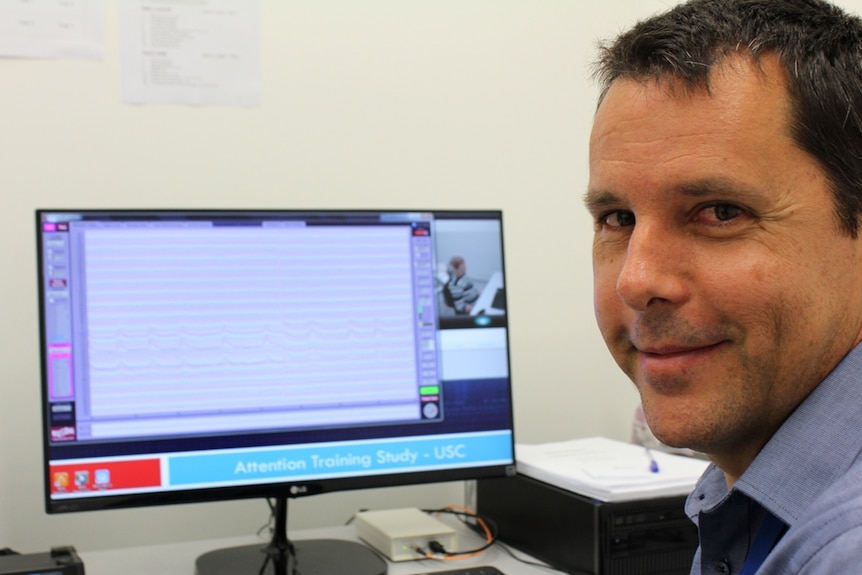 man sits in front of a computer screen showing brain waves.