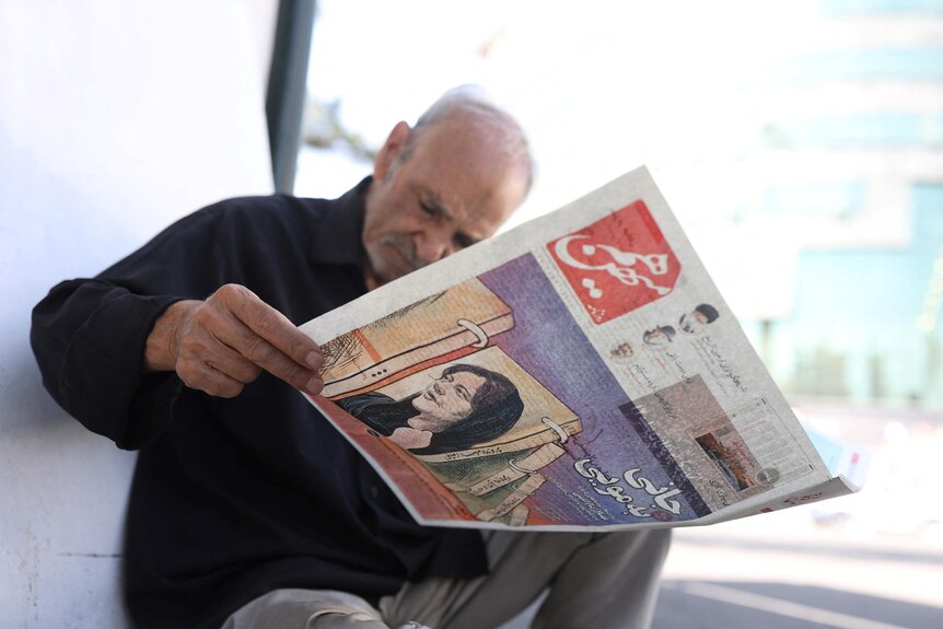 A man reading a newspaper with an image of Mahsa Amini on the cover