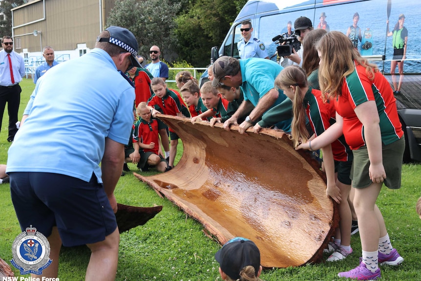 Police and young students hold a hollowed out tree.