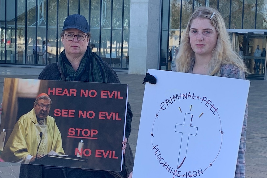 Two women stand with signs condemning George Pell.