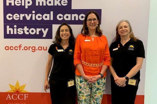 Vicky Darling in an orange blouse next to women in black shirts in front of a cervical cancer banner