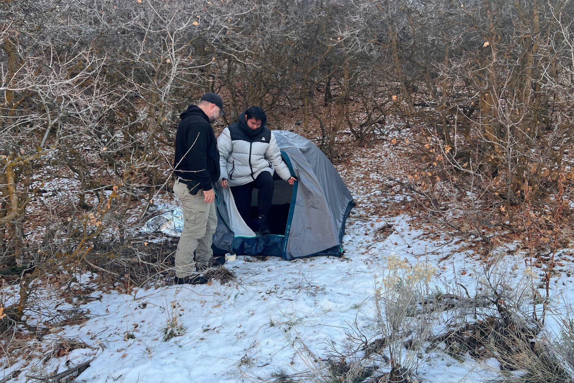 A police officer standing next to a boy coming out of a tent in a forest area. 